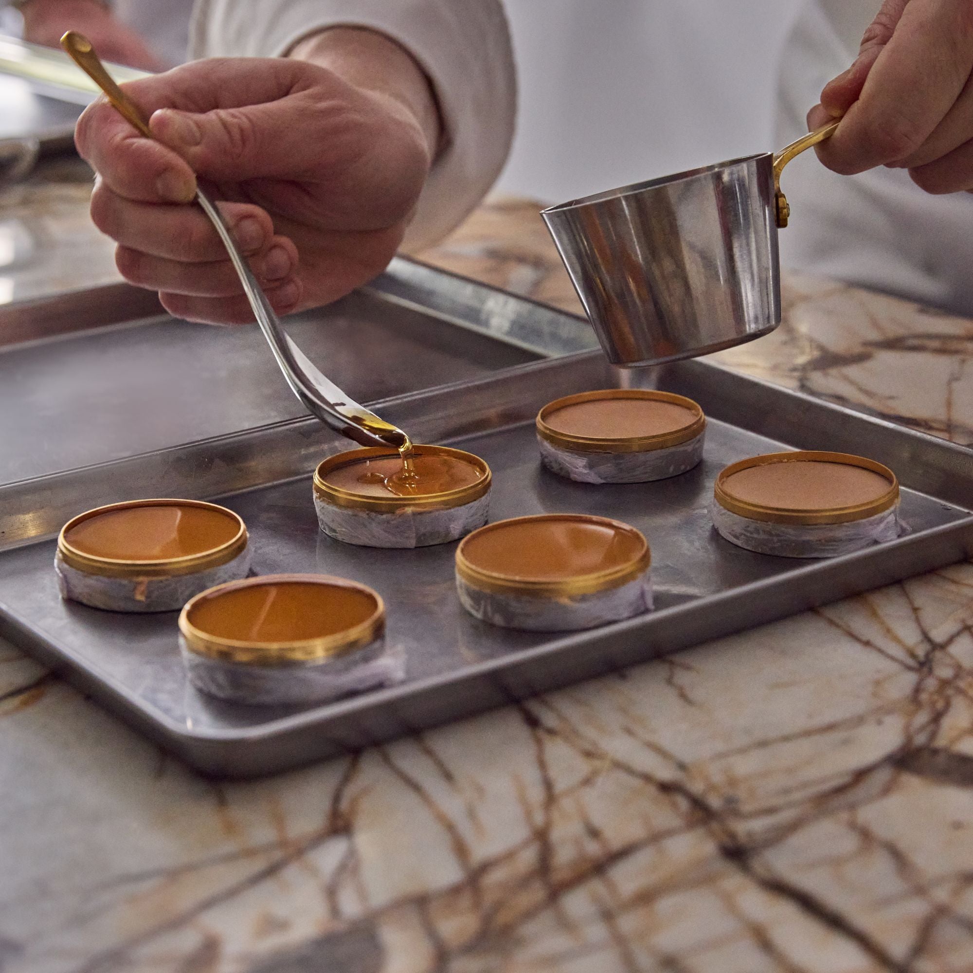 Chef pouring a liquid into stackable ring moulds on a tray.
