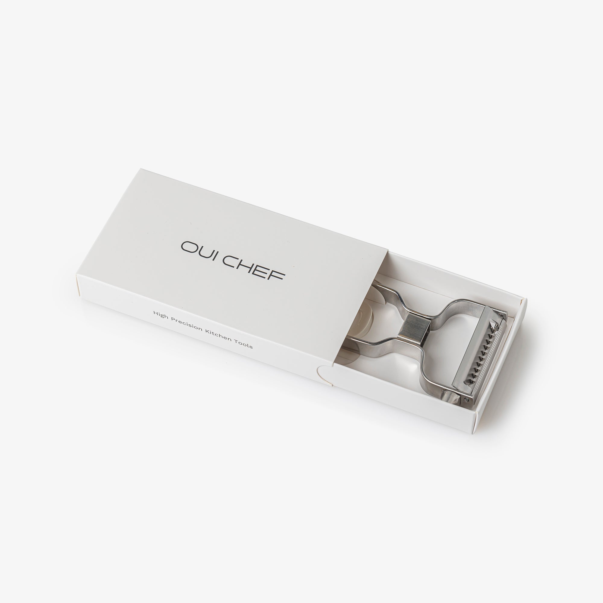 Oui Chef stainless steel julienne peeler displayed in its retail packaging against an off-white background.