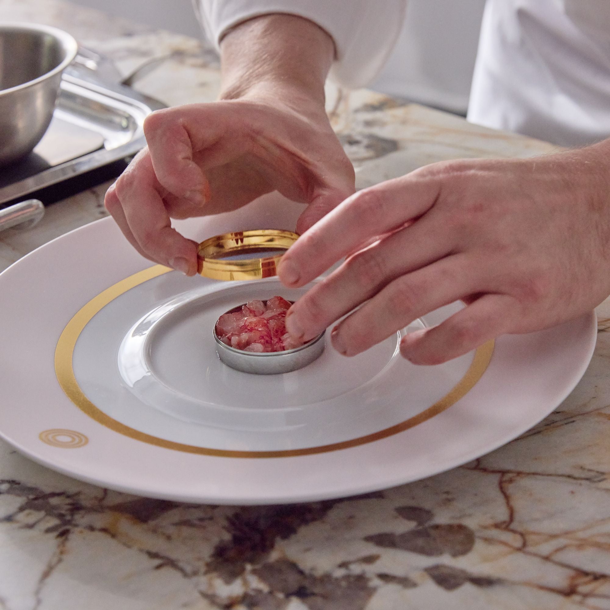 Chef placing the stackable rings on top of the mould base, placed on a white dish which is sitting on a marble countertop. 