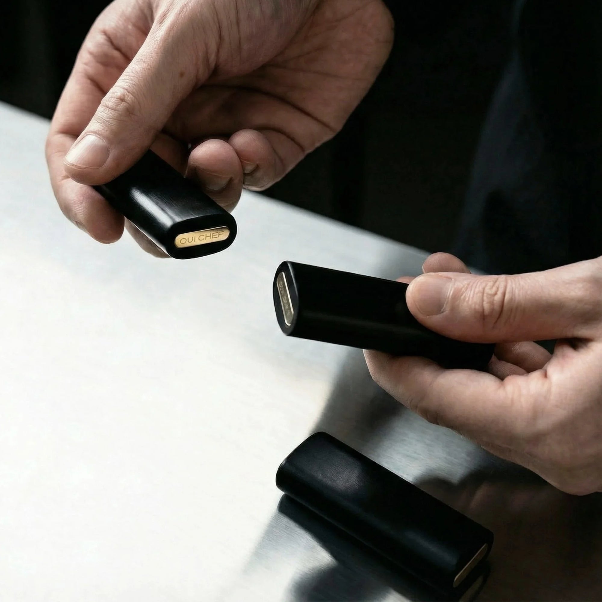 Two hands holding two laylow knife rests  over a steel kitchen worktop.